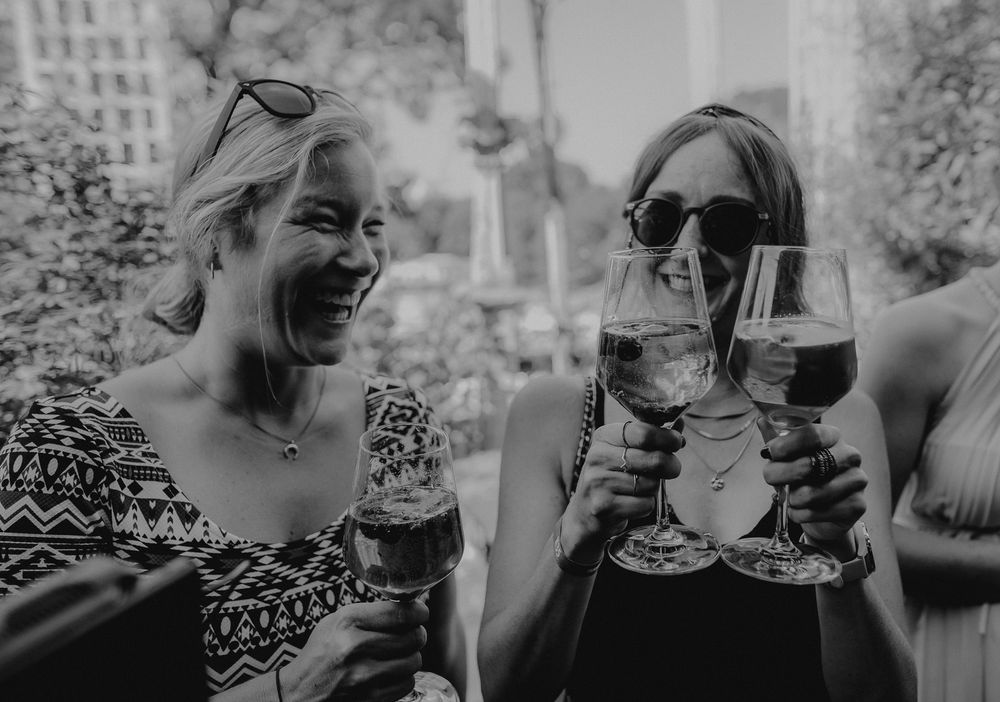 Two people sharing wine and laughter at an outdoor social gathering.