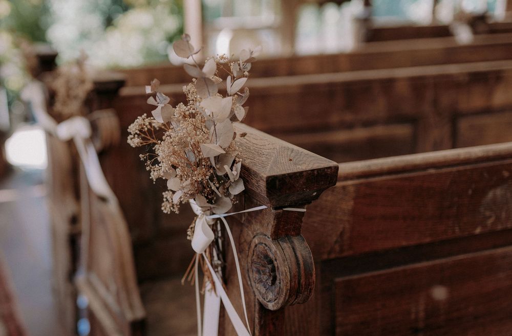 Dried flower arrangement decorating wooden church pew with white ribbon.