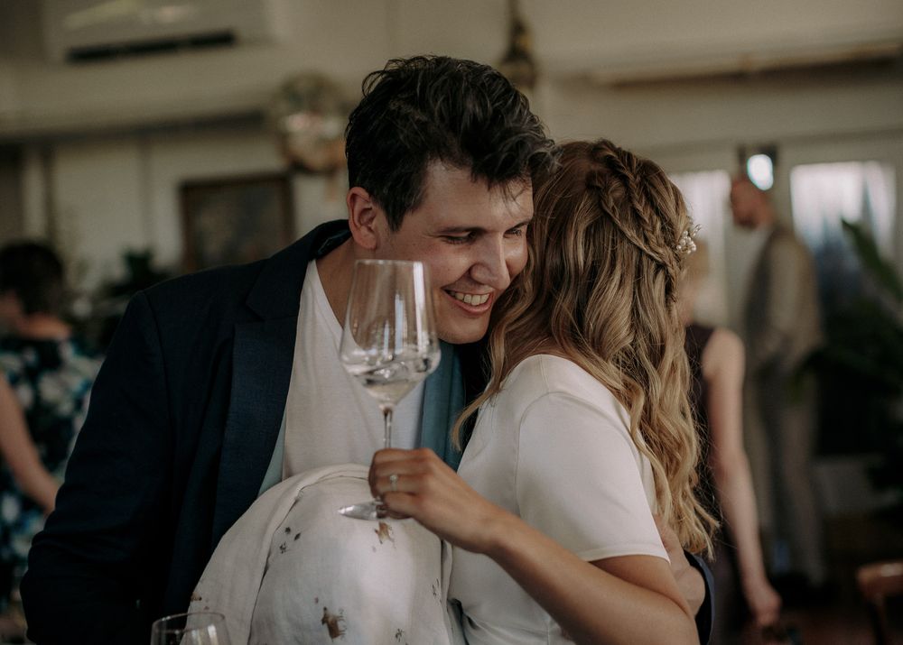 A couple sharing an intimate moment while holding wine glasses at an indoor event.