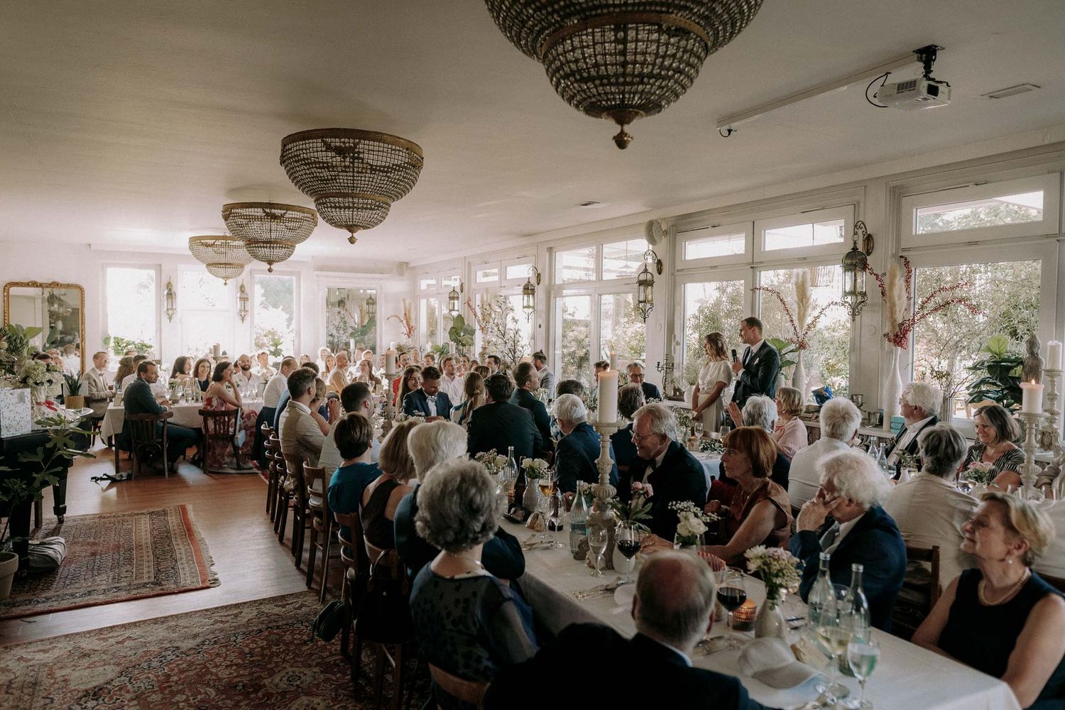 Elegant wedding reception venue with ornate chandeliers and tables filled with celebrating guests.
