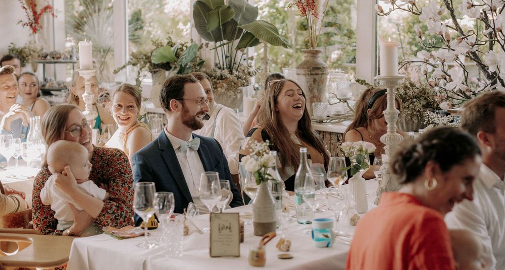 Wedding reception guests laugh and celebrate at decorated indoor venue.
