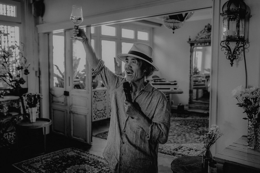 Black and white photo of someone in a hat making a celebratory gesture indoors.