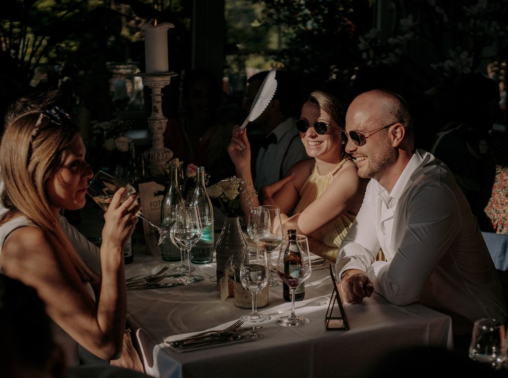 Wedding guests enjoy drinks and conversation at an outdoor reception table.