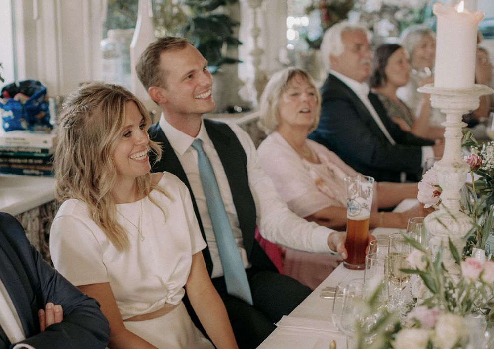 Wedding guests seated at a reception table share joyful laughter during celebrations.