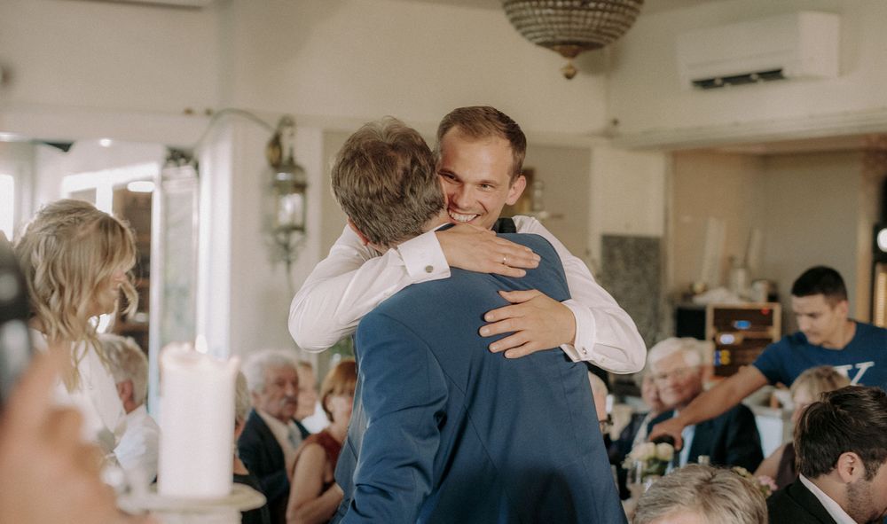 Two people share an emotional embrace during a celebration in a bright reception hall.