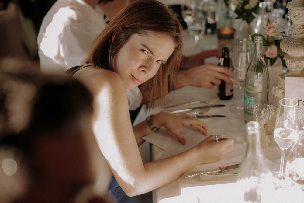 A guest in formal attire leans over a white-clothed dining table during an event.