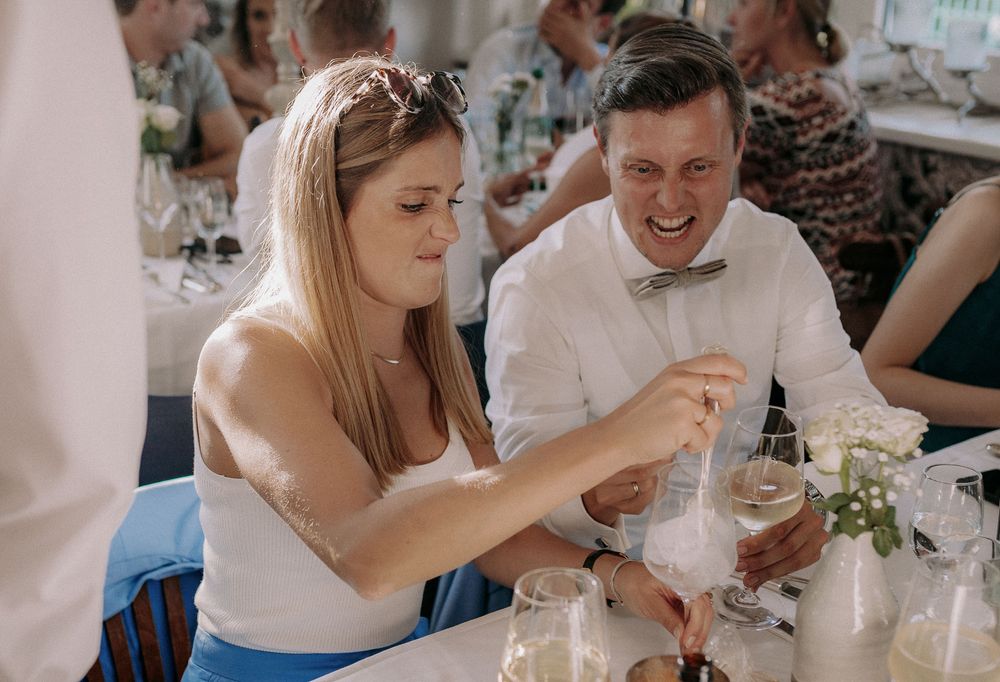 Two wedding guests share a lighthearted moment while examining drinks at their table.