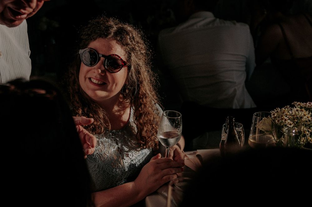 A guest wearing sunglasses holds a wine glass while enjoying a reception celebration.