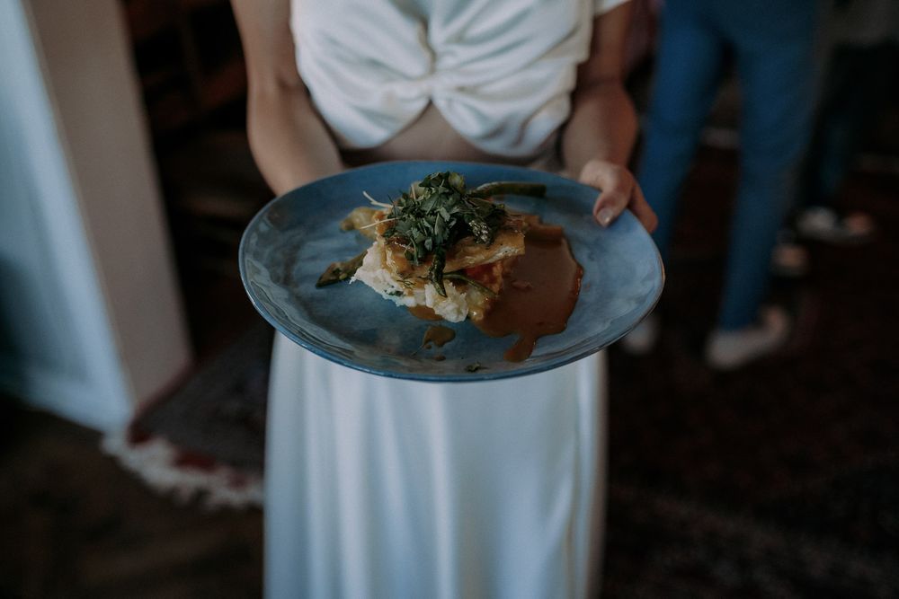 A plated meal with garnish being served on a white plate against a dark background.