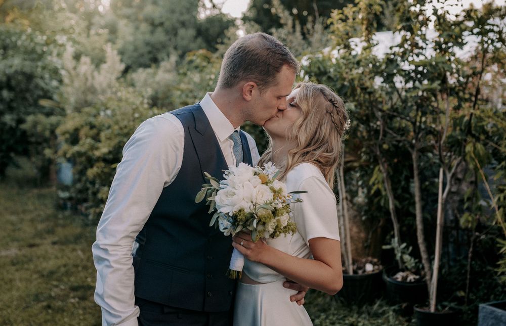 A romantic wedding moment captured in a garden setting with white floral bouquet.