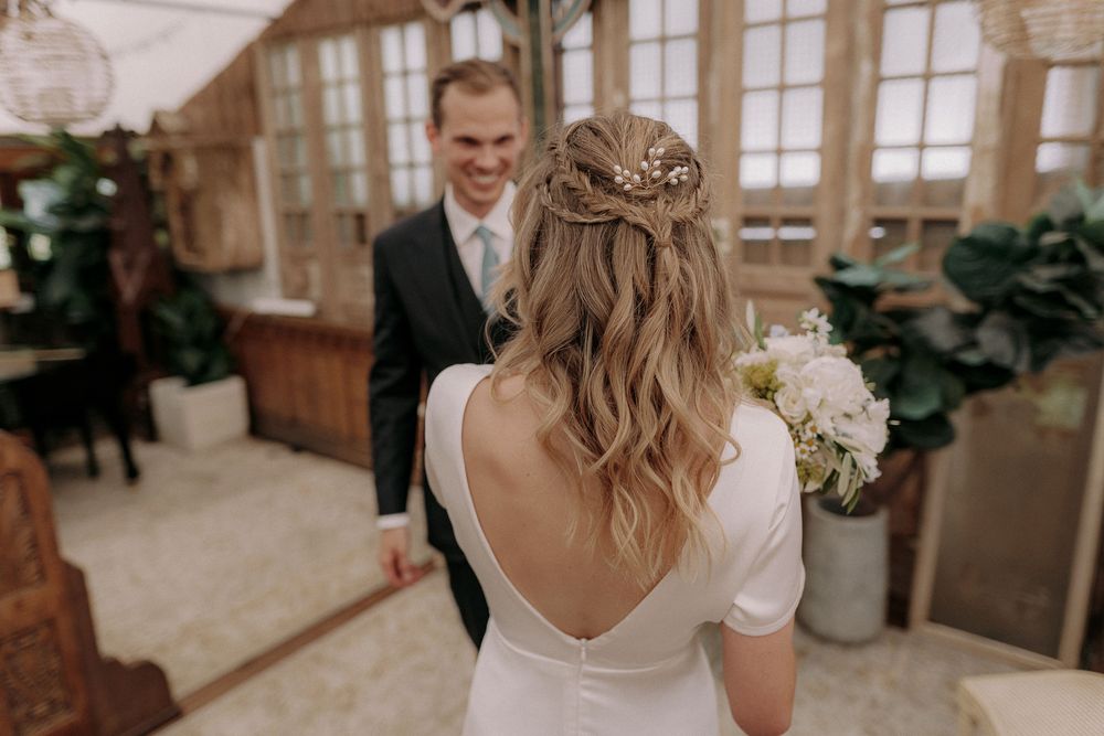 Back view of bride's hairstyle and dress with groom in background.