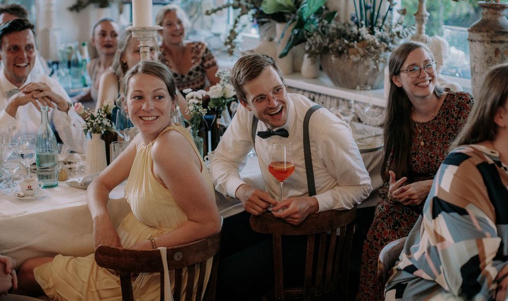 Wedding reception guests enjoying drinks and laughter at decorated dining tables.