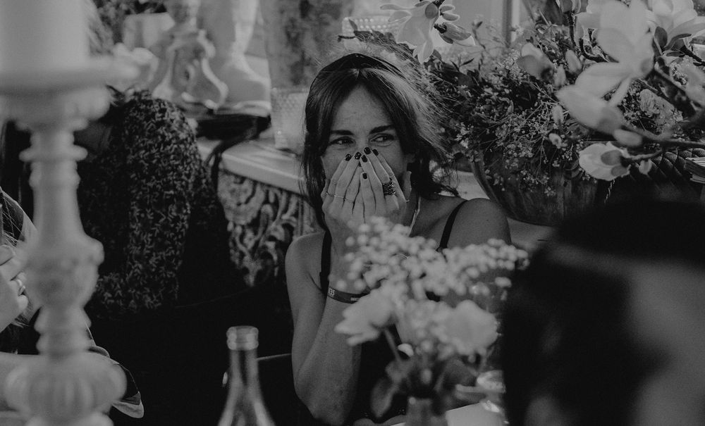 A candid black and white photograph of a guest at an elegant dinner party surrounded by flowers and wine bottles.