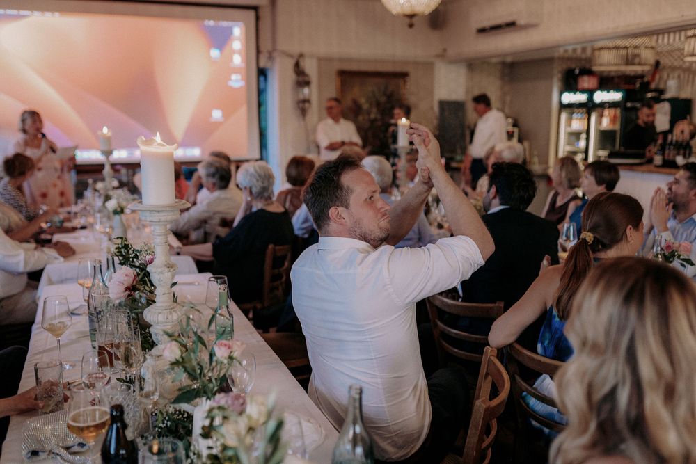 Wedding guests raising their glasses during a toast at an indoor reception with elegant table decorations.