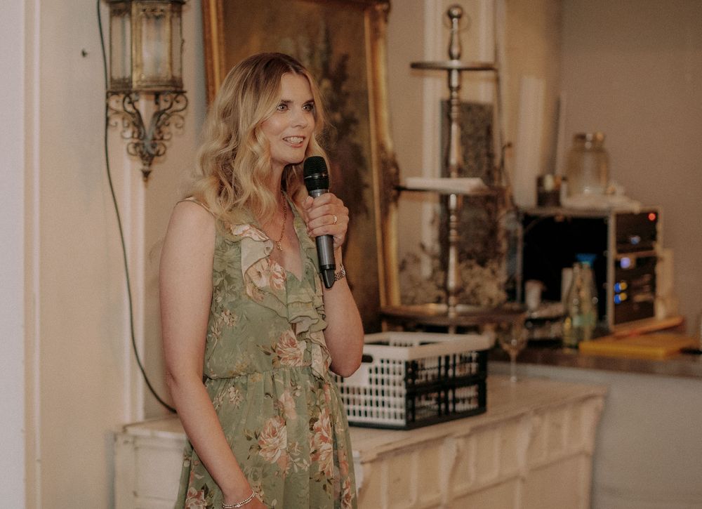 A speaker holds a microphone during an event in an elegantly decorated venue with ornate lighting.
