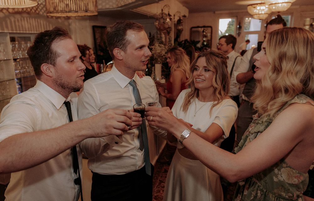 Guests toasting with drinks at an indoor celebration with warm lighting.