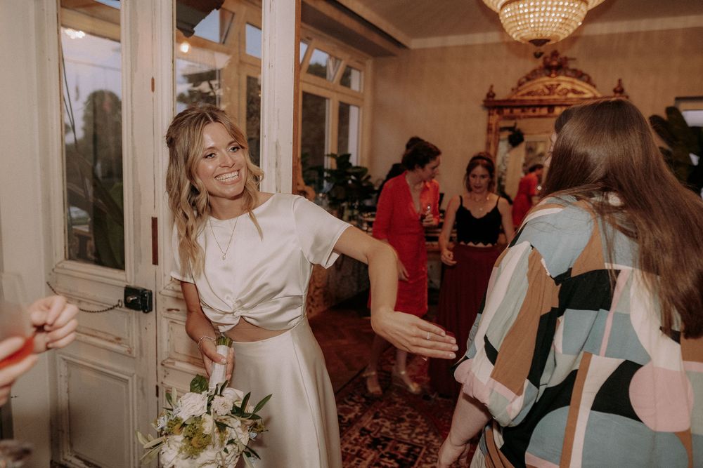 A wedding celebration in an elegant room with a chandelier and ornate mirror as guests gather on a red carpet.