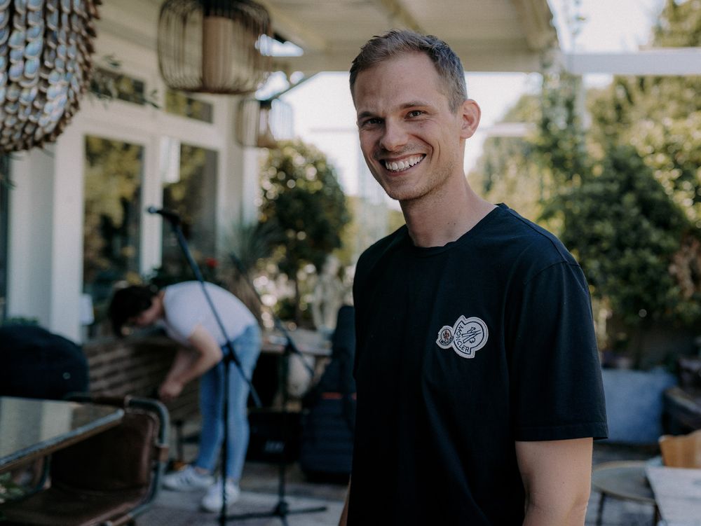 Man in black t-shirt smiling on outdoor patio.
