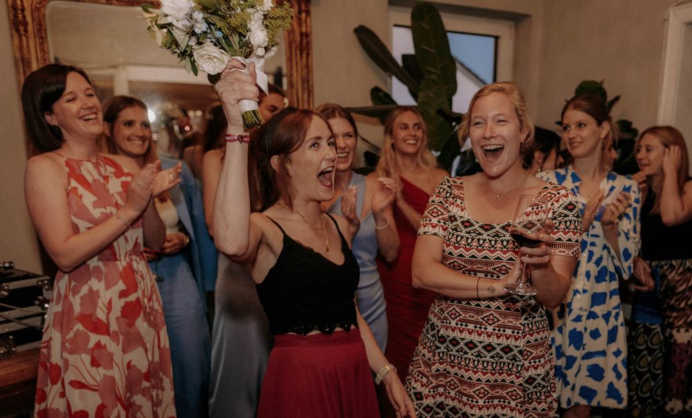 Wedding guests in colorful dresses laugh and celebrate during a reception party.