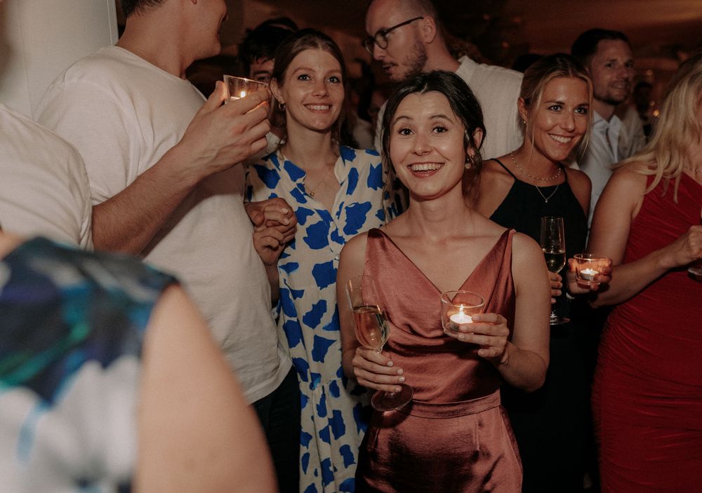 Wedding reception guests in formal attire enjoying drinks and conversation in an elegant venue.