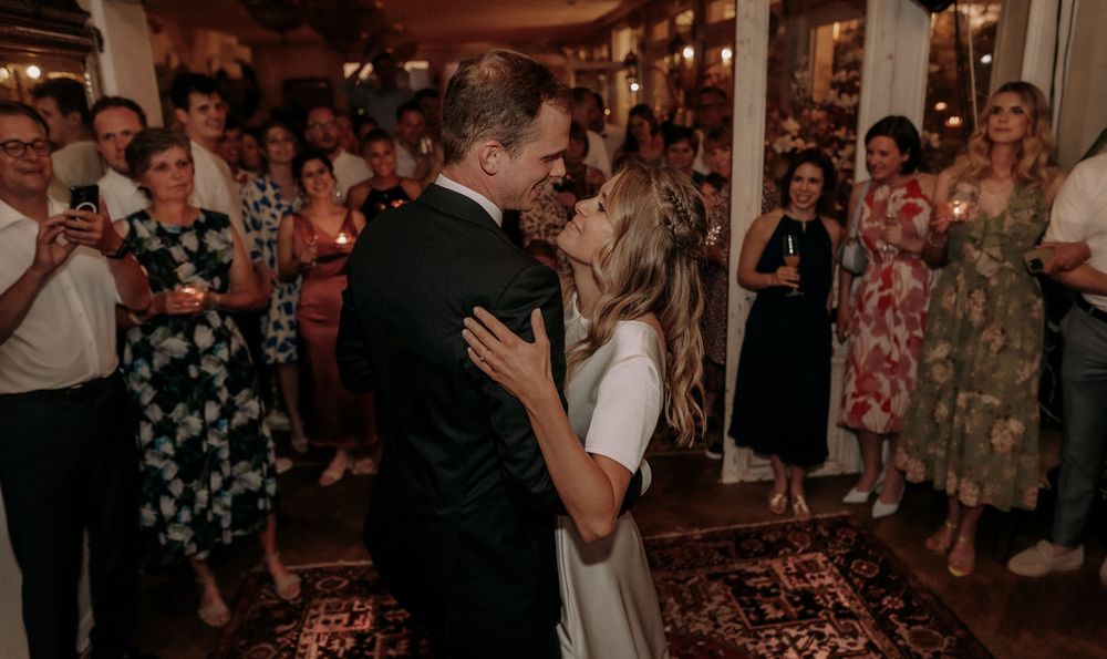 A couple's first dance at their wedding reception surrounded by guests with phones capturing the moment.