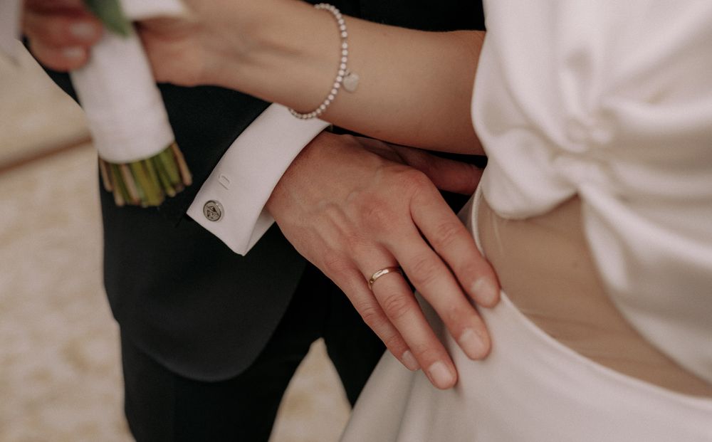 Close-up of hands showing wedding rings and bracelet details against formal attire.
