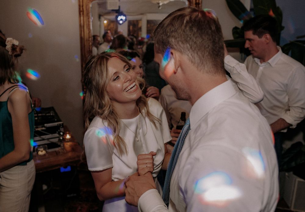Couple dancing together under colorful party lights at reception.