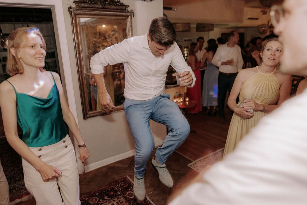 Party guests dancing energetically at an indoor gathering with decorative wall art.
