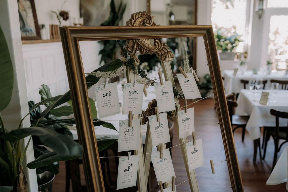 Wedding seating chart displayed in vintage gold frame with hanging name cards.