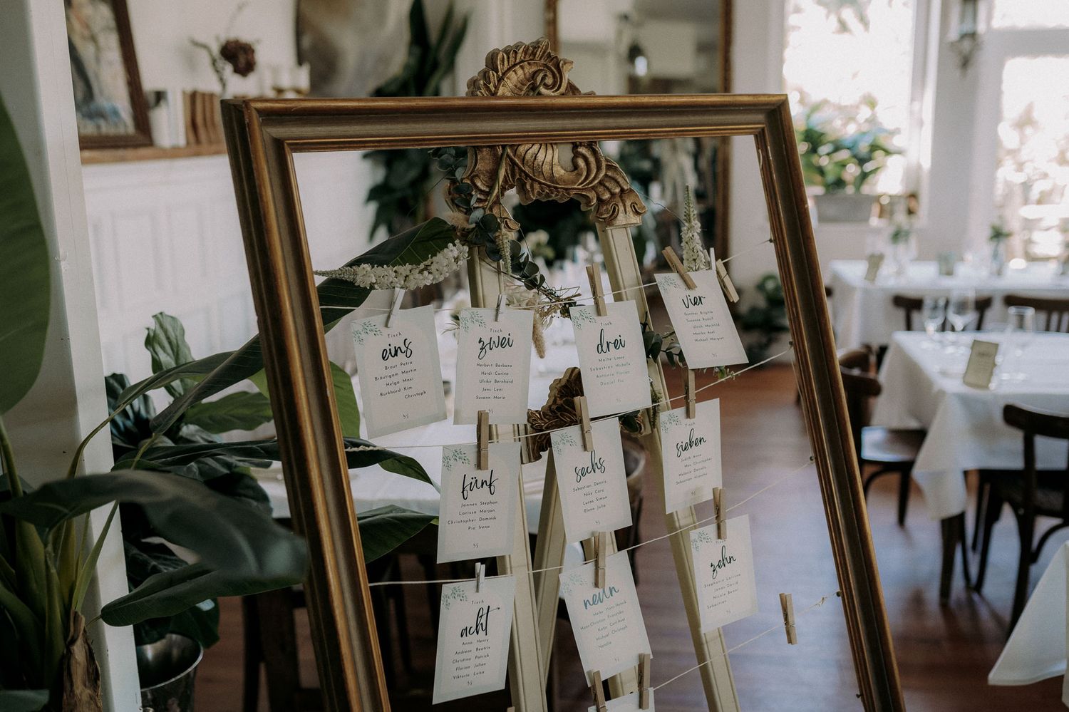 Wedding seating chart displayed in vintage gold frame with hanging name cards.