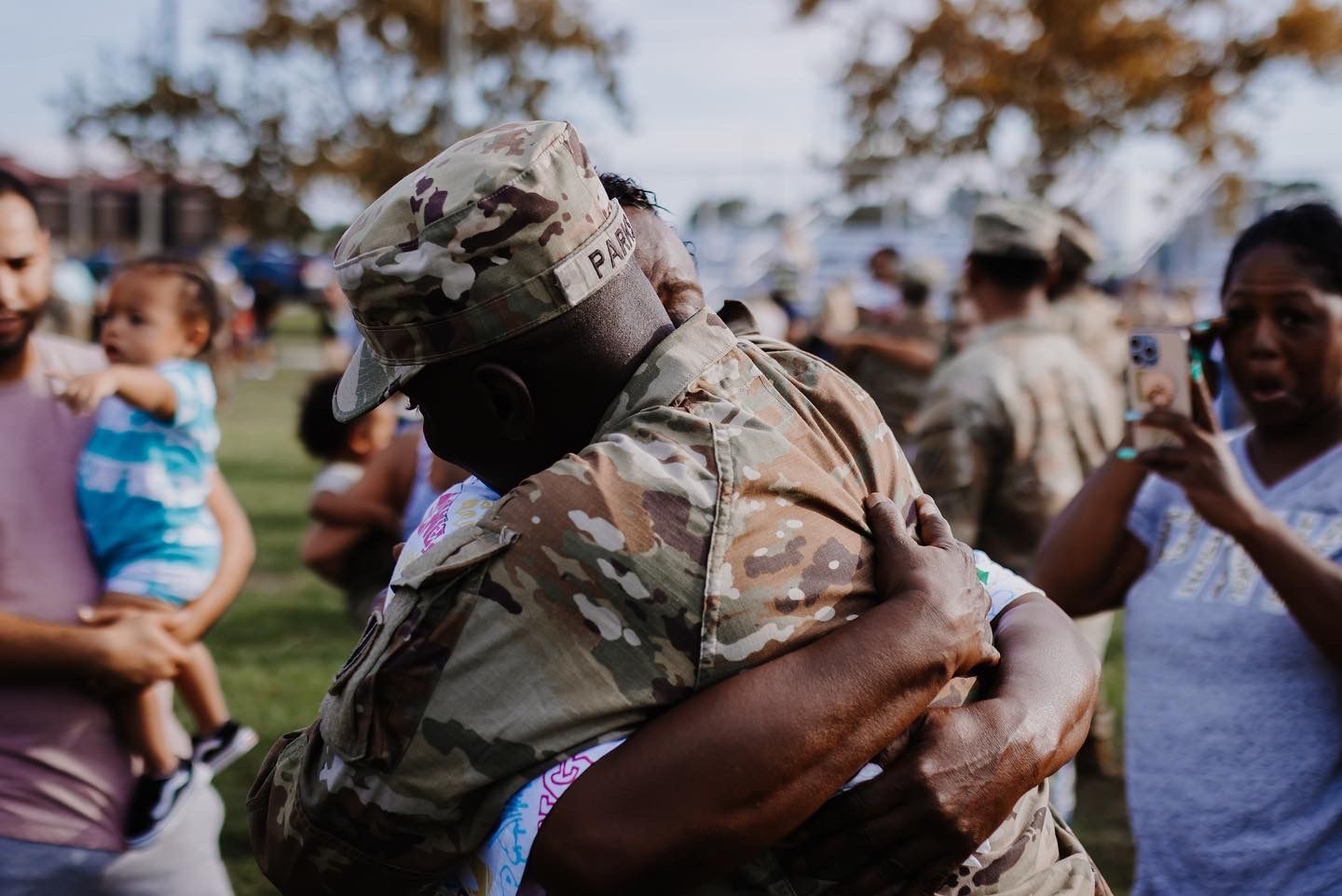 Emotional military homecoming reunion in a crowded outdoor park.