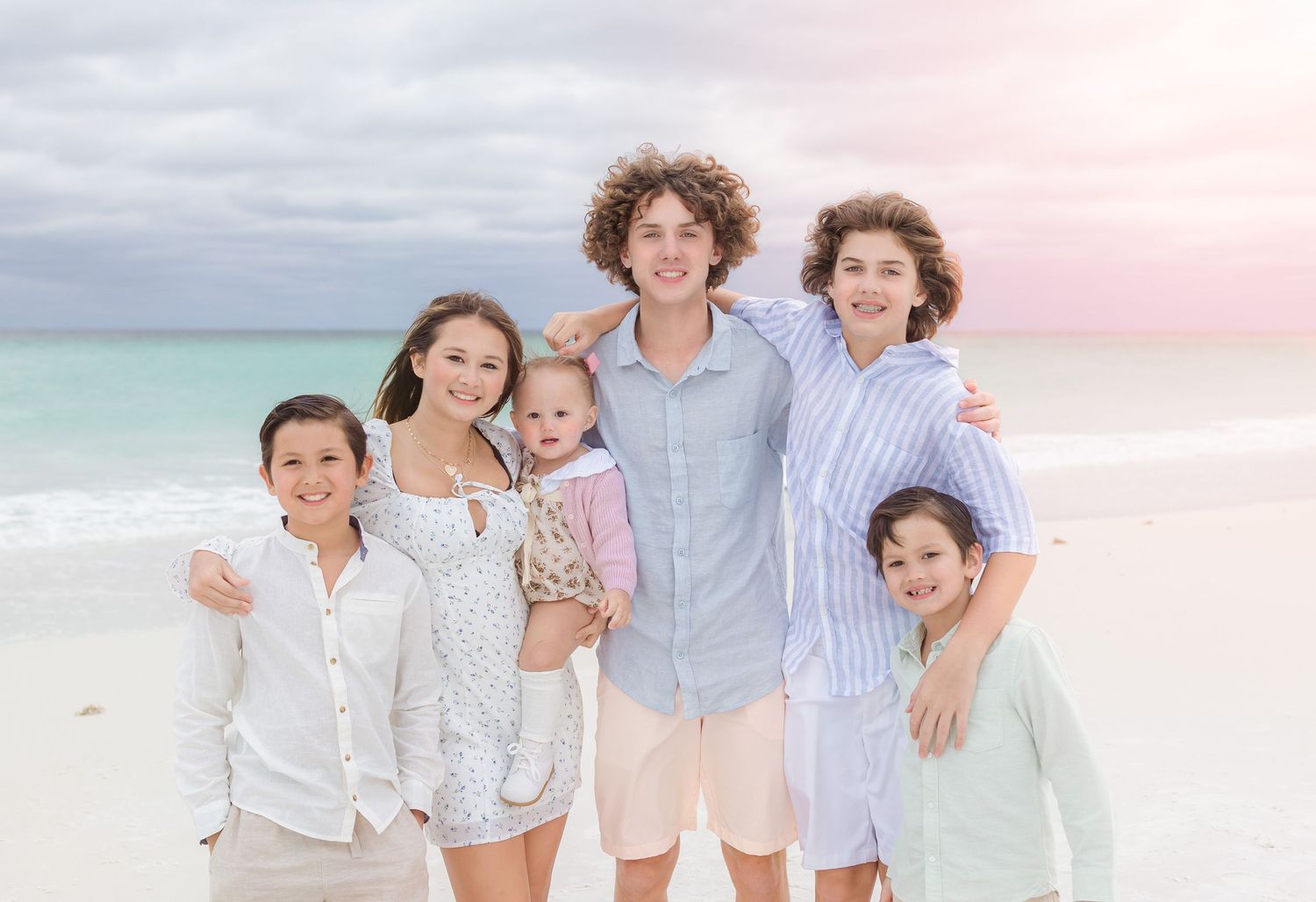 Happy family in light casual clothing posing together on beach at sunset.