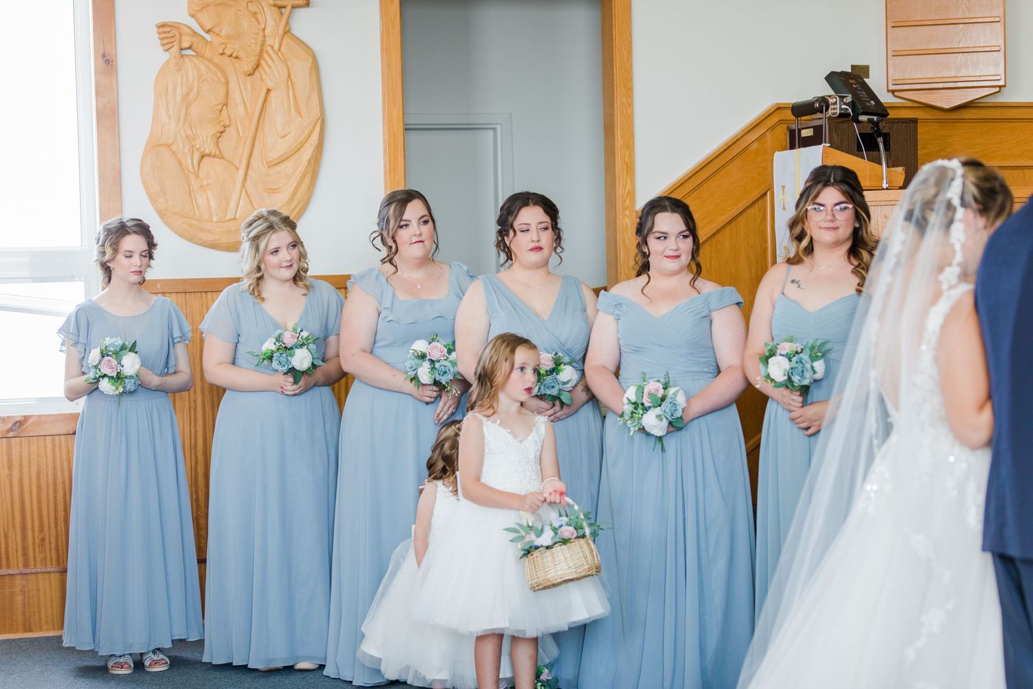 Bridesmaids in matching blue dresses gather with flower girl before the ceremony.