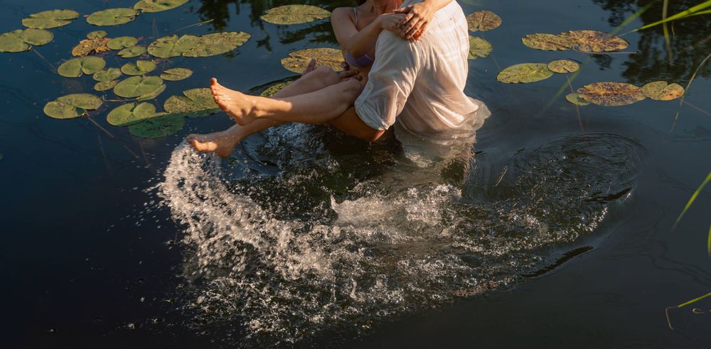 Water splashes around a couple as they play in a lily pad covered pond.
