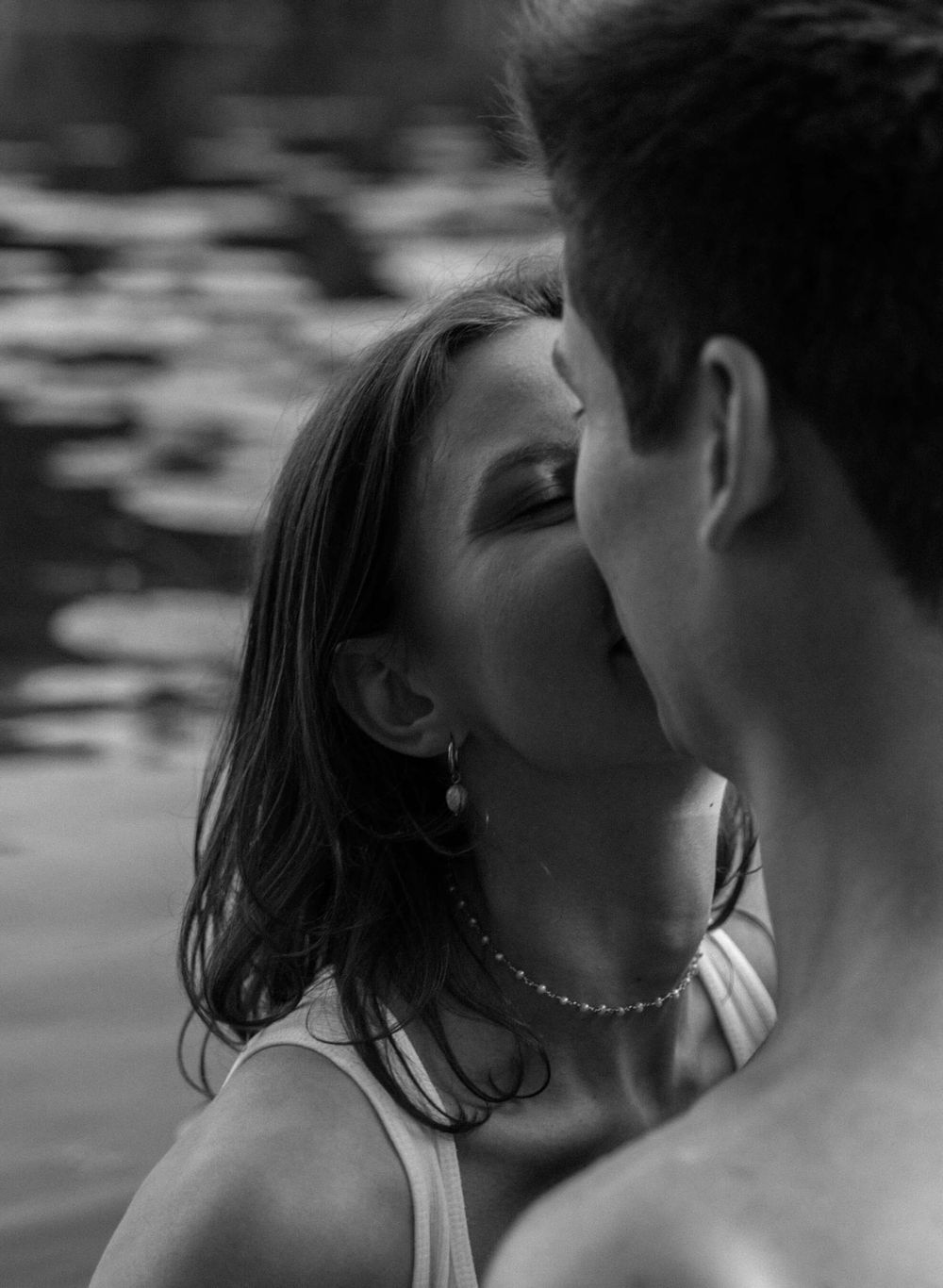 Black and white intimate portrait of couple near water with lily pads in background.