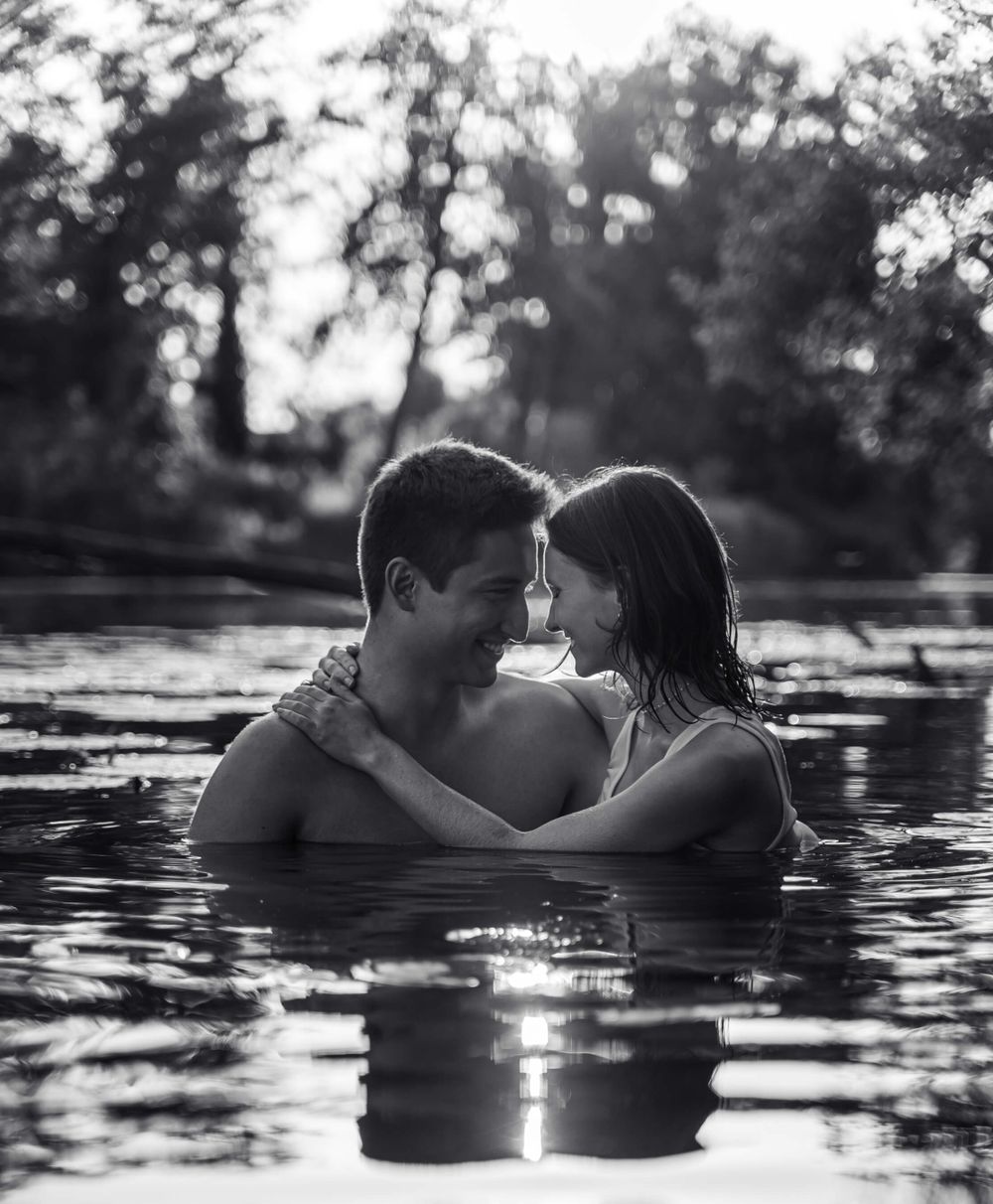 Black and white photo of couple embracing in water with reflective ripples surrounding them.