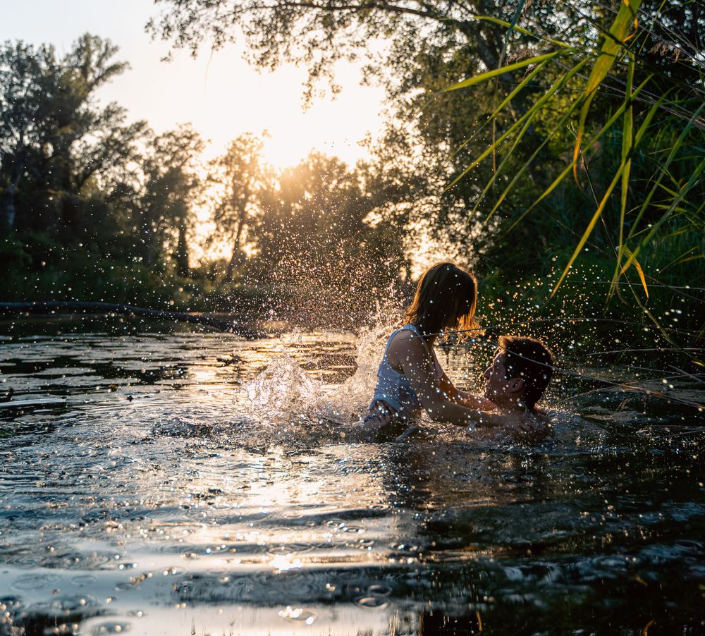 Couple splashing playfully in water during sunset with backlit water droplets.