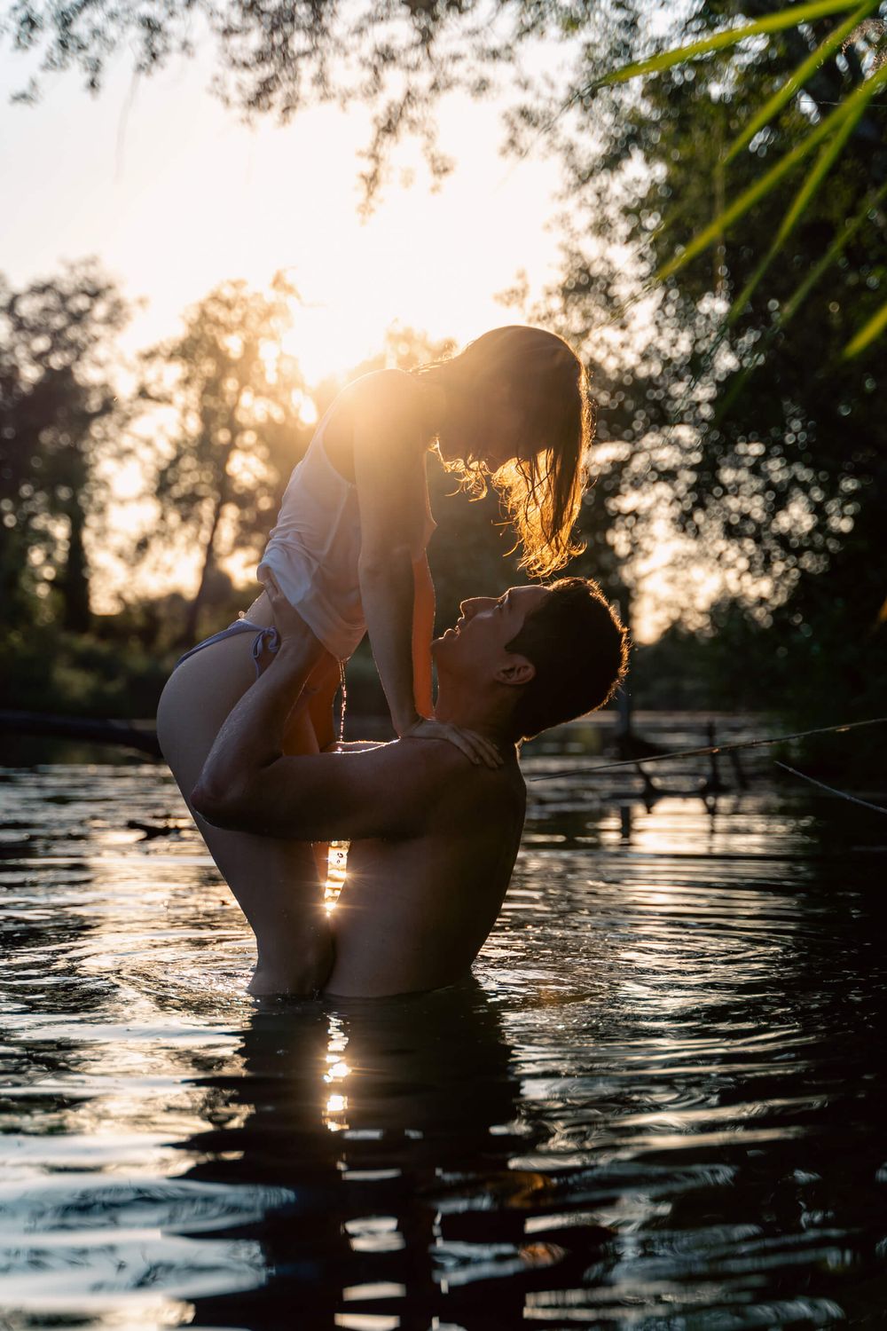 Silhouetted couple shares romantic moment in water during golden sunset.