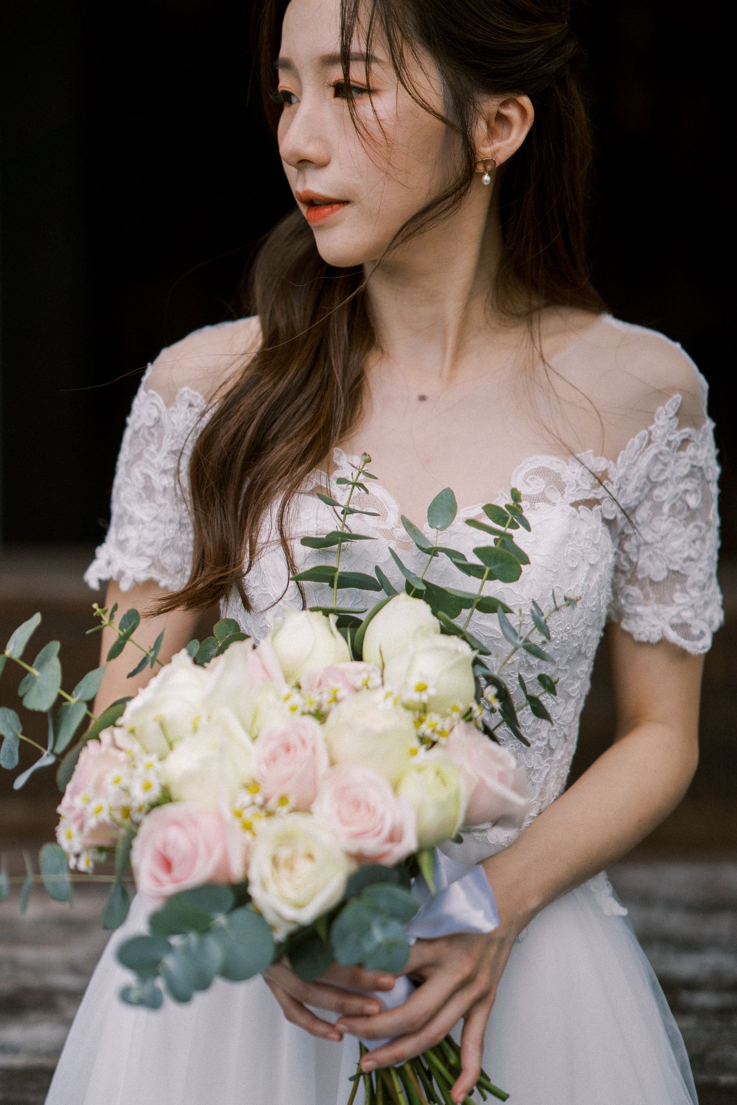 Delicate white lace wedding dress with soft pink and white rose bouquet.