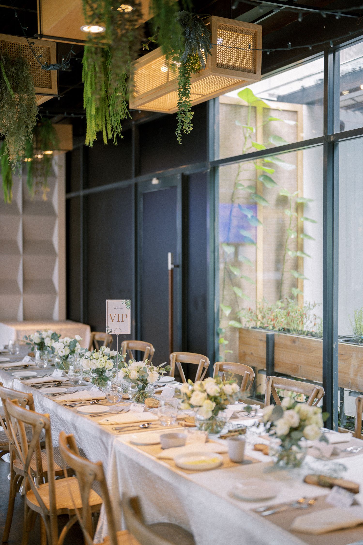 Modern wedding reception venue with floor-to-ceiling windows and hanging greenery decorations.