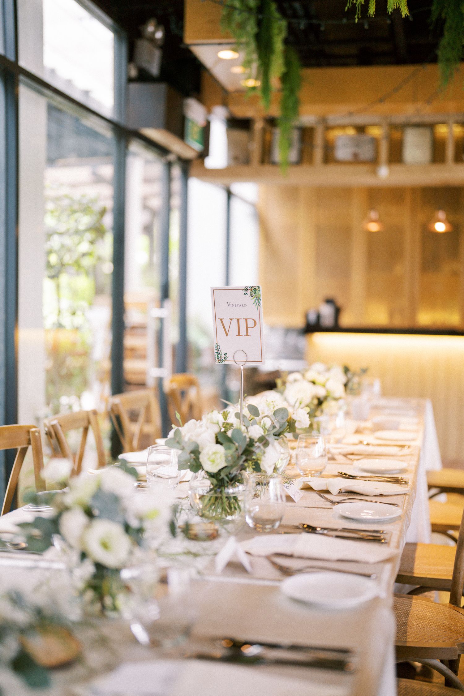 White table settings with VIP sign and delicate floral arrangements in a light-filled venue.