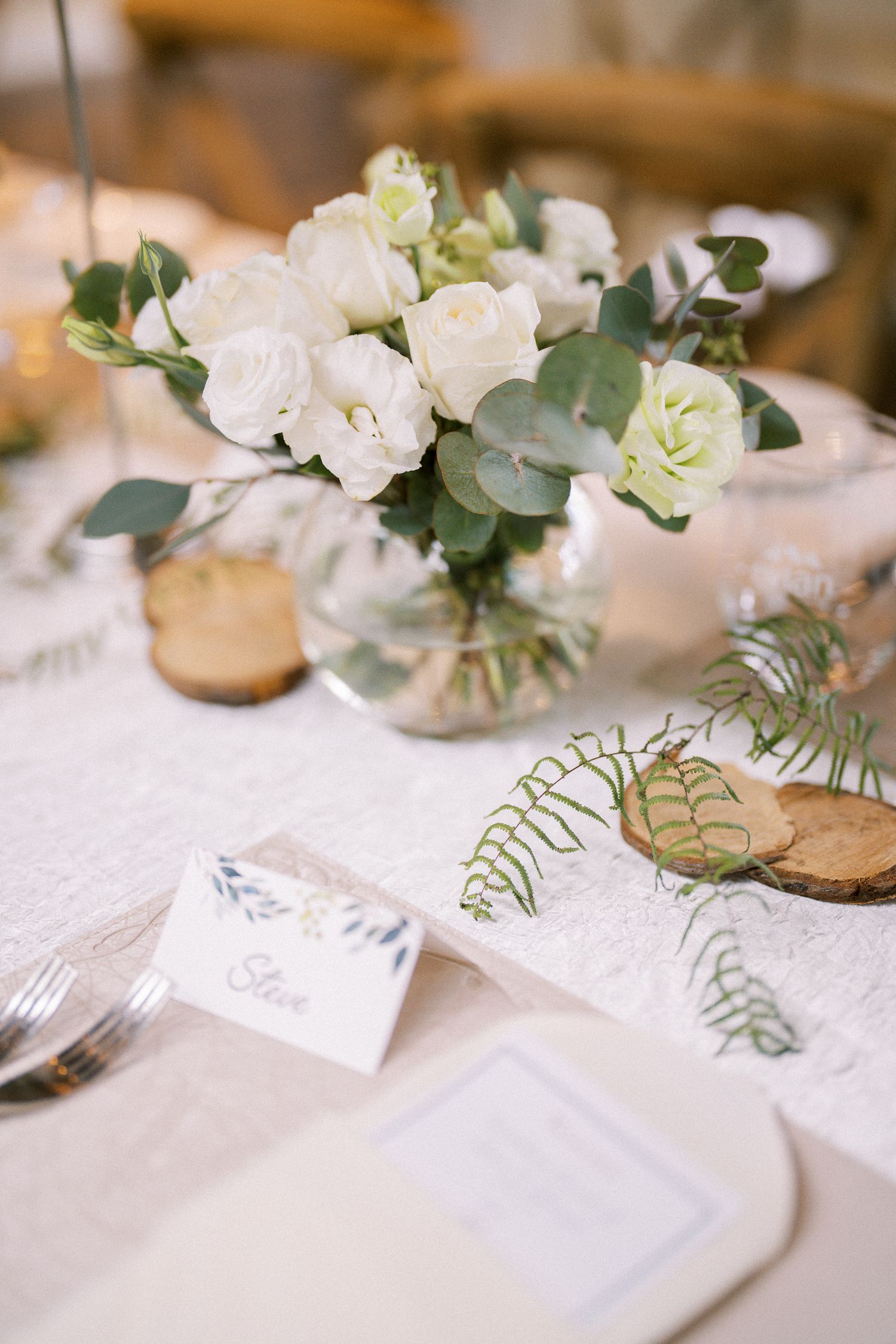 Close-up of white floral centerpieces with eucalyptus leaves on elegant table settings.