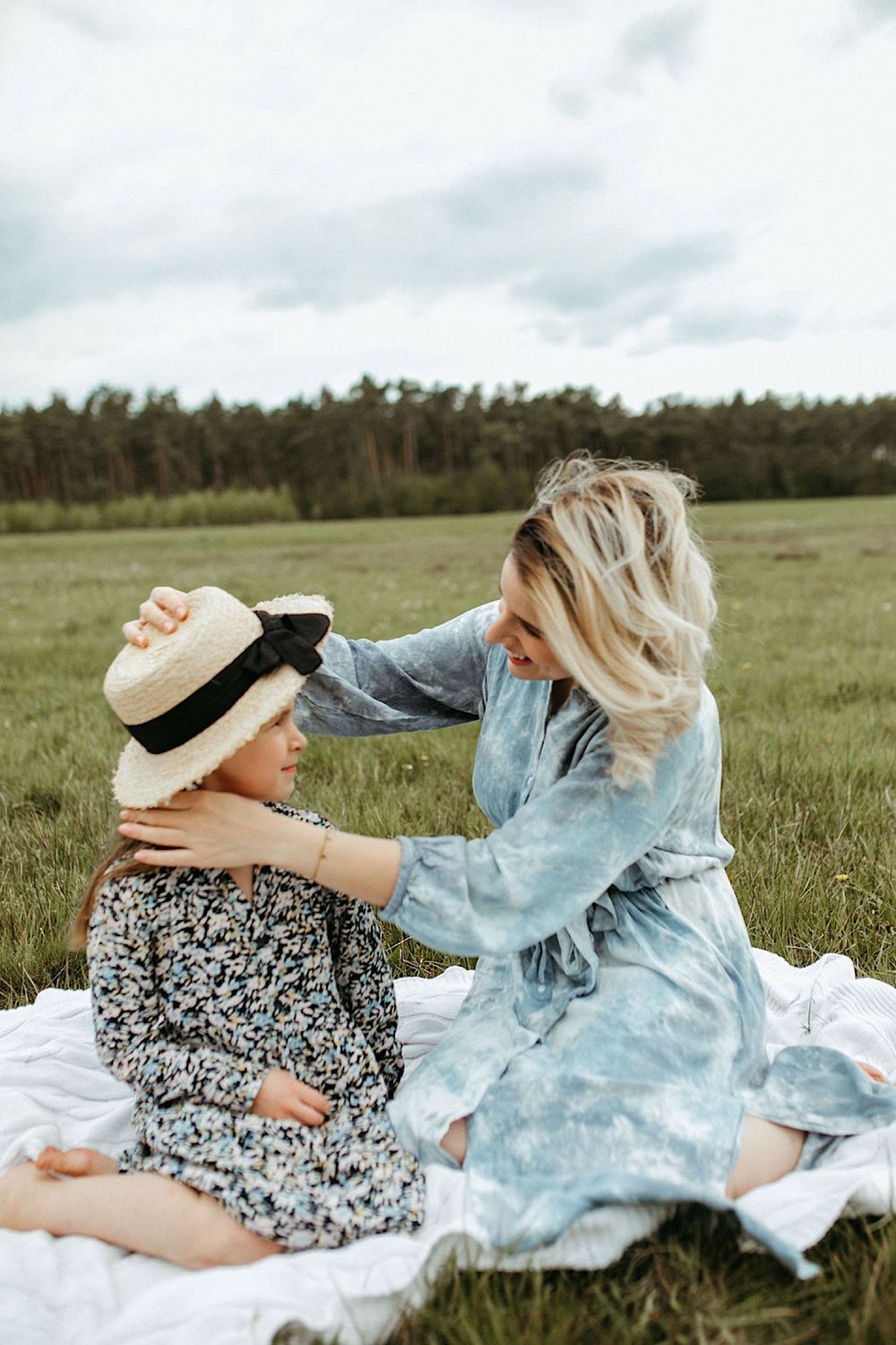 Two people in casual clothes laying on white blanket in grassy field.