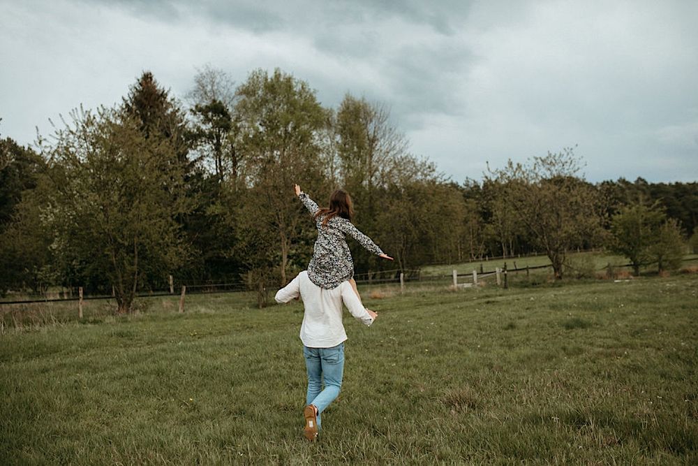People running and playing in an open green field with forest backdrop.