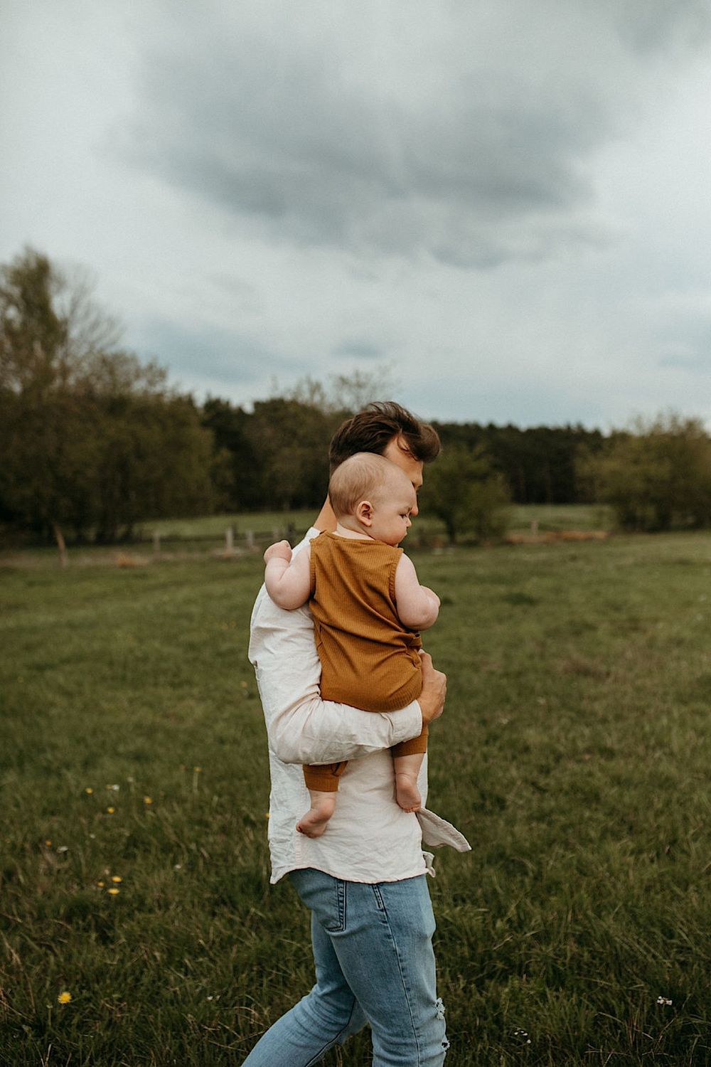 Candid photos of parent carrying child in brown outfit across grassy field.
