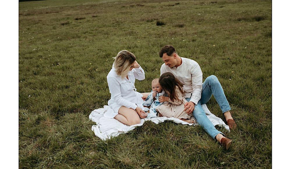 Family relaxing together on blanket in open field during photo session.