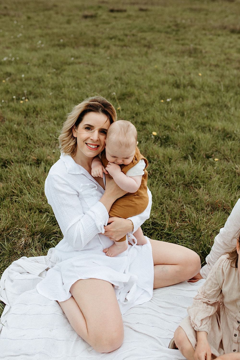 Family portrait session on white blanket in grassy field on cloudy day.