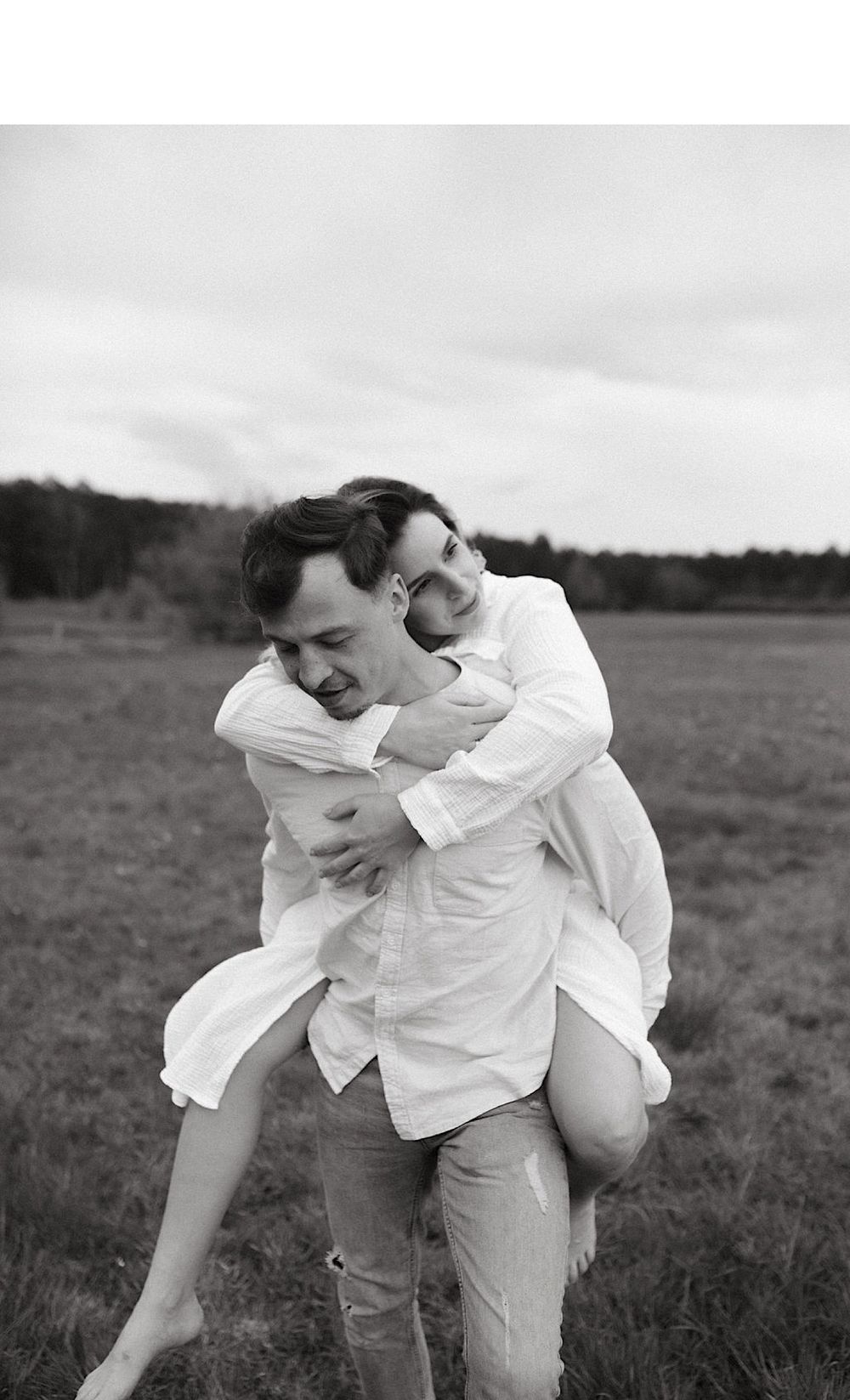 A couple shares a lighthearted moment while playing piggyback in a grassy field.