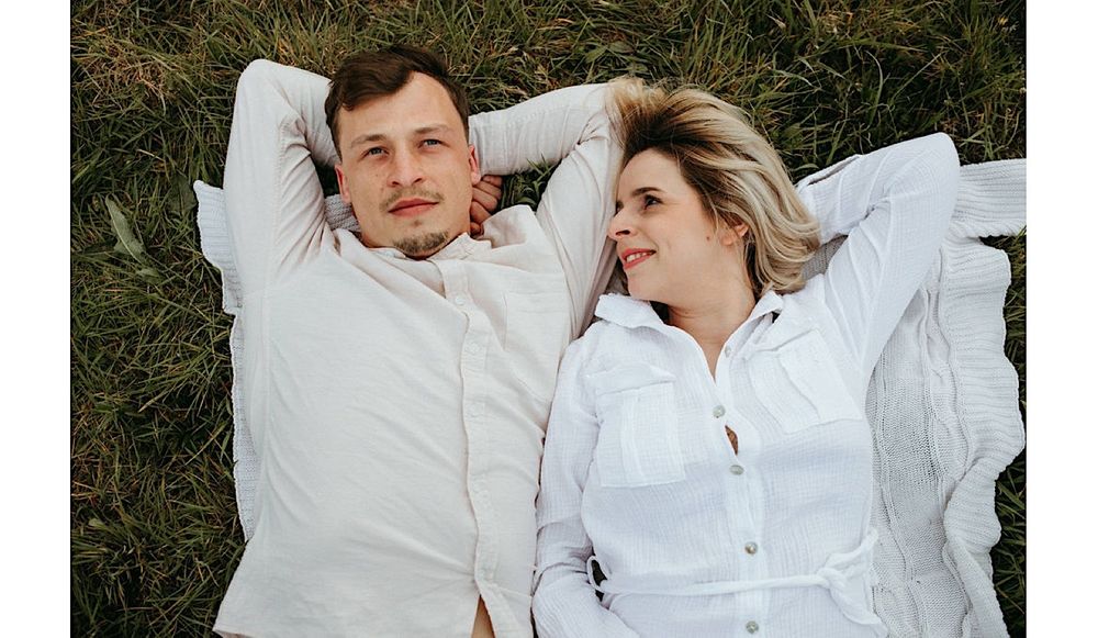 A couple lying in the grass sharing an intimate moment outdoors.