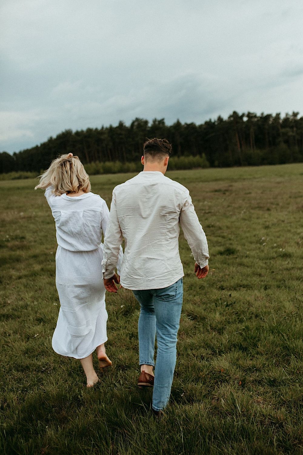 Two people in white shirts running together through a scenic meadow.
